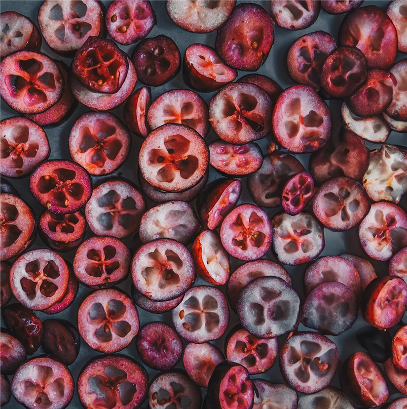 Close-up of sliced cranberries showing their characteristic internal star pattern in various shades of deep red and pink against a dark background, highlighting a key natural ingredient in UTI prevention supplements.