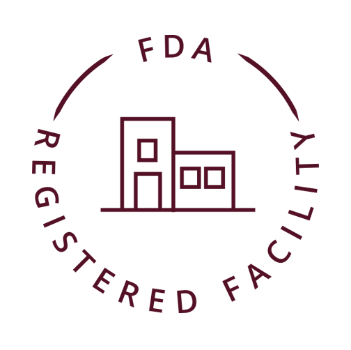 A product certification badge with minimalist design on a beige background. It features a simple line drawing of buildings in a circular emblem with the text 'FDA REGISTERED FACILITY' curved around the top. Below the emblem, the text 'fda registered facility' appears in an elegant italic font.