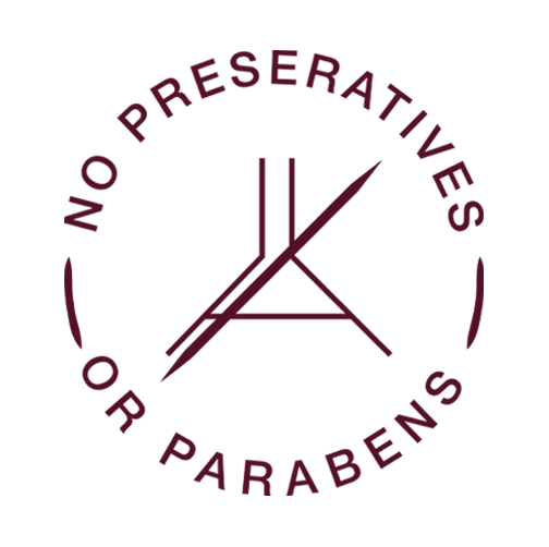 A product ingredient badge on a beige background featuring a circular emblem with a crossed-out utensil symbol. The text 'NO PRESERVATIVES OR PARABENS' curves around the circle. Below the emblem, the text 'no preservatives, gluten, or parabens' appears in an italic font.