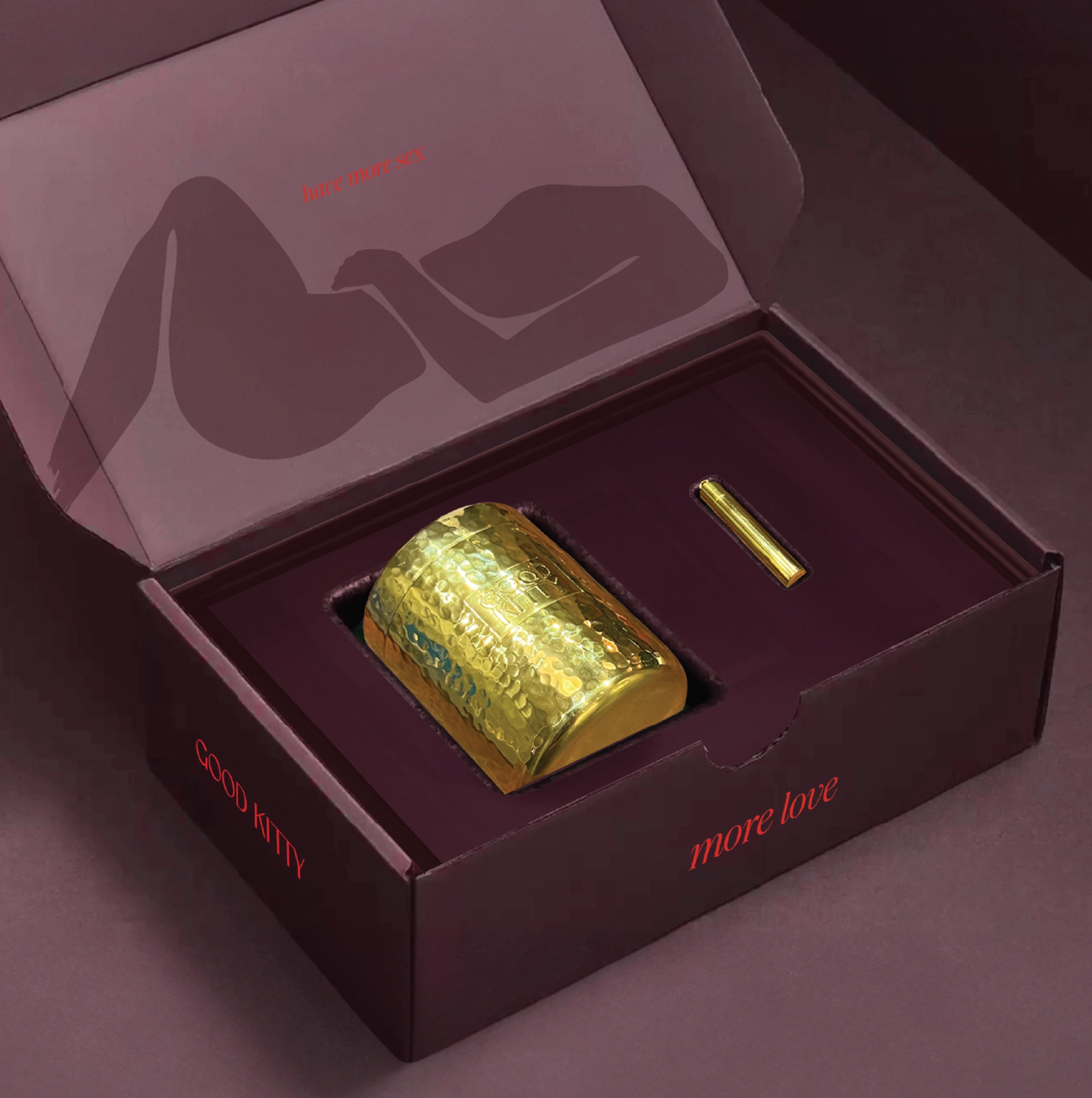 Artistic photograph of the UTI Biome Shield Starter kit featuring a luxurious refillable brass-clad stainless steel canister and 24K Overnighter Pendant designed by Meghan Carozza for sustainable Good Kitty UTI prevention and women's sexual wellness. Open burgundy gift box displaying a hammered gold Good Kitty container and gold pill key, with 'more love' text on the box and a silhouette of a reclining figure on the interior lid, showcasing the brand's elegant packaging.