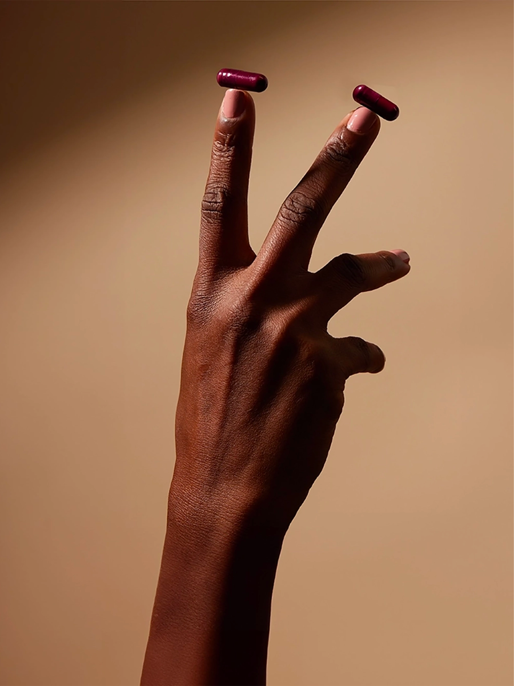 Close-up of a Black hand holding two burgundy UTI Biome Shield capsules between fingers against a warm beige background. The word 'bioactives' appears vertically along the left side with an 'our science' button below.