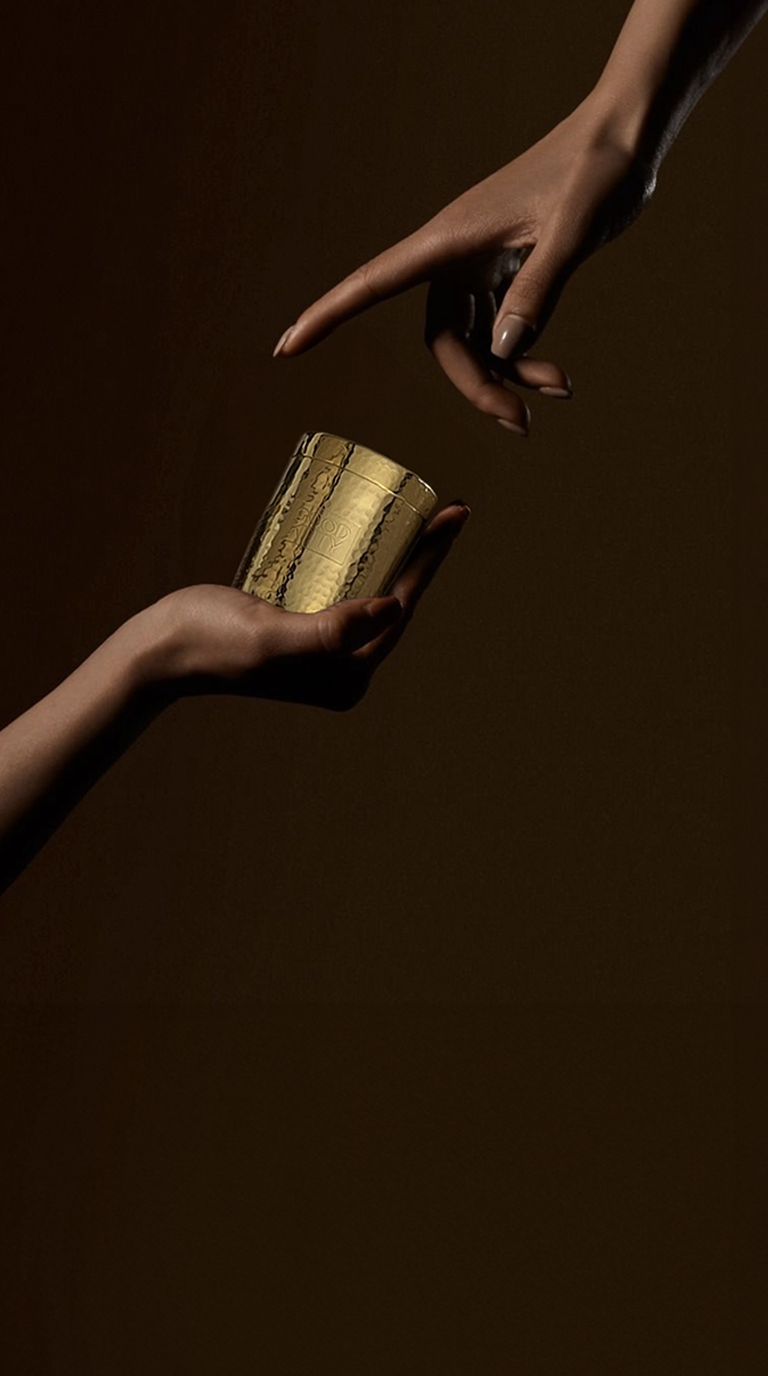 Two hands reaching toward a gold Good Kitty capsule vessel on a dark background.
