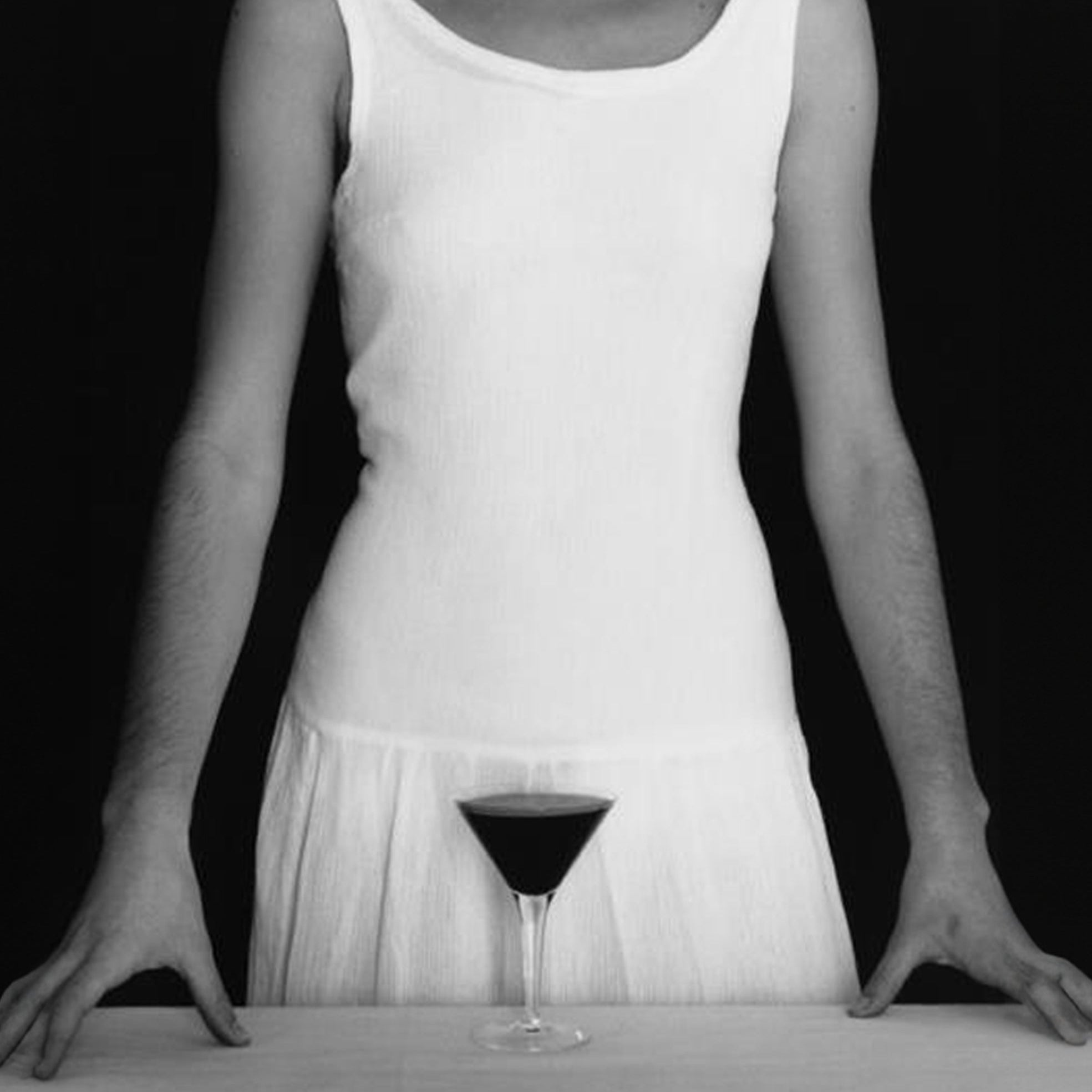 Person wearing a white dress with a glass of red wine on a black background
