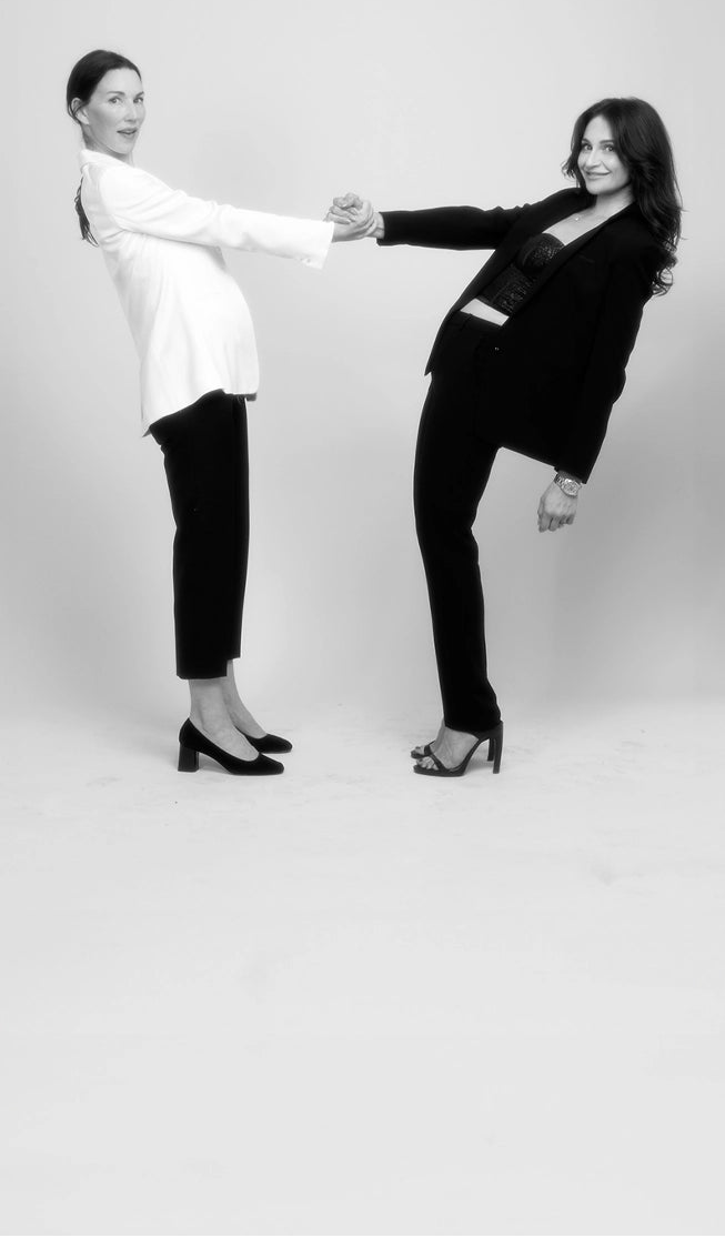 Two women holding hands and leaning back against a plain background.