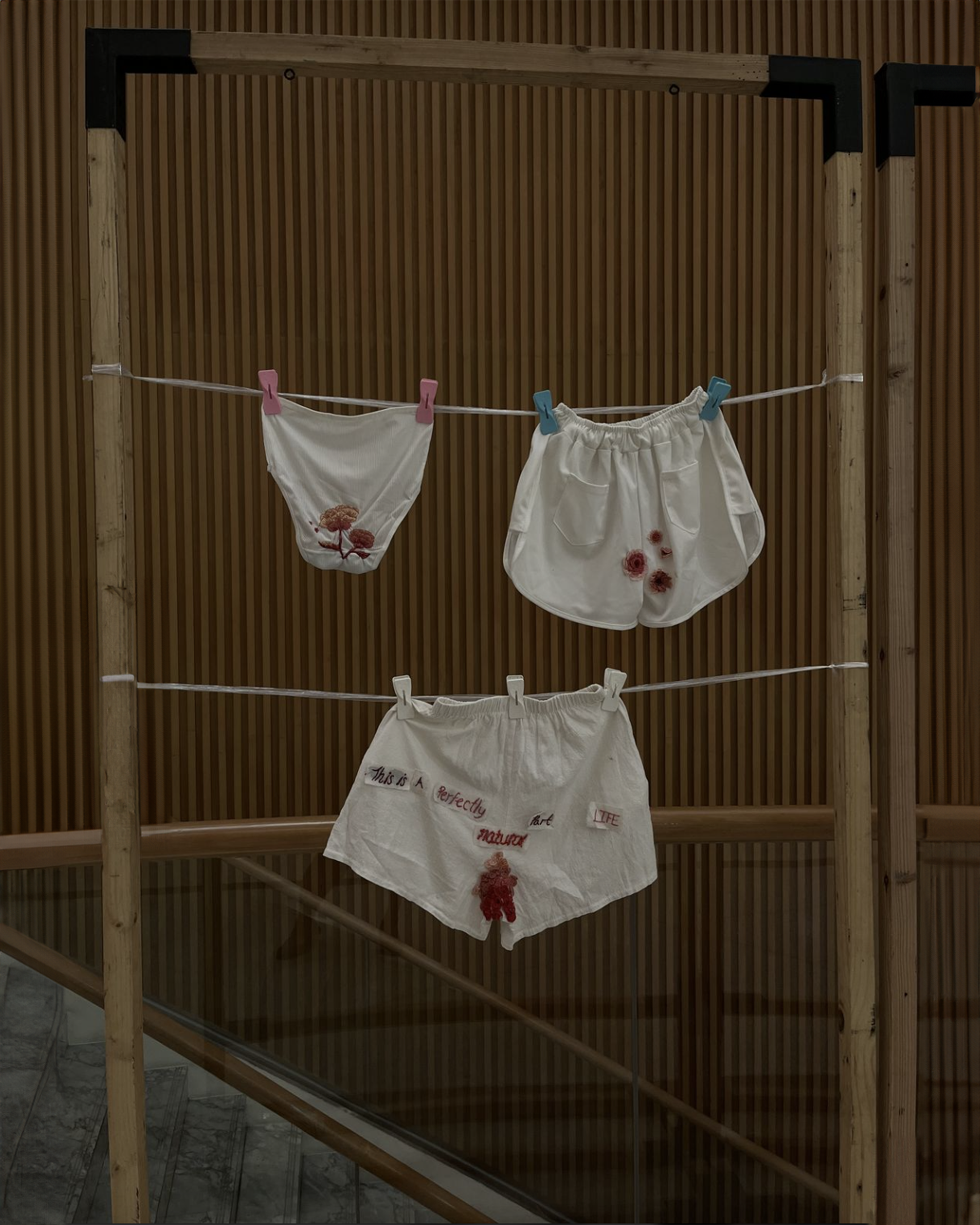 Three pairs of white underwear with red stains hanging on a clothesline against a wooden wall.