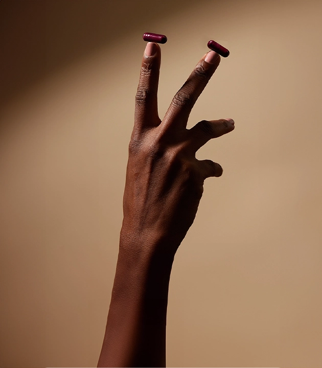 Split-screen homepage design Close-up of a Black hand holding two burgundy UTI supplement capsules on fingertips against a warm neutral background. Good Kitty logo at top with white text overlay reading 'non-antibiotic uti prevention' and 'we call it magic but really it's science'