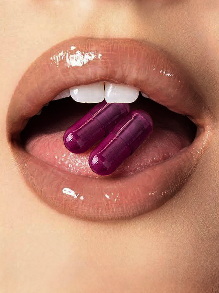 Close-up of glossy lips with two purple capsules or pills held between the front teeth. The vibrant purple supplements contrast against natural-toned lips with a slight shine, showcasing the product in an artistic, stylized manner.